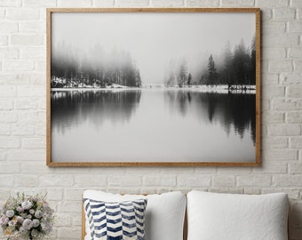 May include: A white couch with two pillows, one with a blue and white chevron pattern. The couch is in front of a white brick wall with a framed black and white photograph of a foggy lake and trees hanging above it.