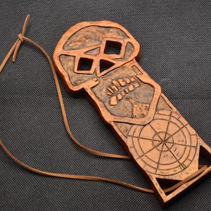 May include: A wooden skull pendant with a compass design on the back. The pendant is attached to a brown leather cord.