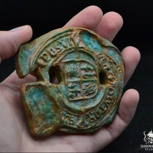 Könnte beinhalten: Ein verwittertes, kreisförmiges Objekt in Bronzefarbe mit einem Schildemblem und dem Text "POST OFFICE HOLLAND". Das Objekt hat ein gealtertes Aussehen mit grüner und orangefarbener Patina. Das Design umfasst einen kreisförmigen Rand mit Text.