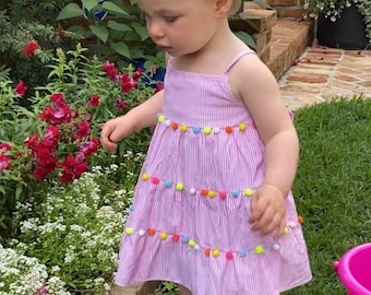 Adorable PomPom sundress for baby girls and toddlers. The dress ties int he back with a sash.