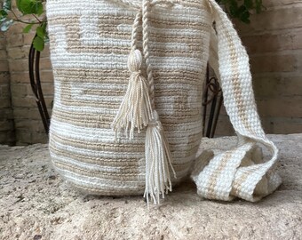 May include: A white and beige crocheted bag with a long strap and tassels. The bag is made of a soft, natural material and has a simple, elegant design.