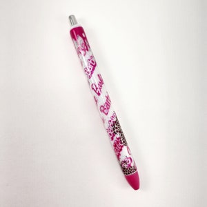 May include: A pink and white pen with a silver top and a glitter finish. The pen has the word "Barbie" printed on it multiple times.