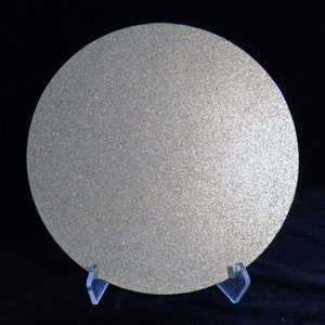 May include: A round, silver-colored sanding disc with a textured surface. The disc is on a clear plastic stand.
