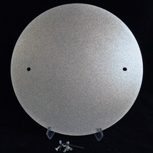 May include: A silver-colored, round, metal disc with two small holes. The disc is textured and has a slightly rough surface.