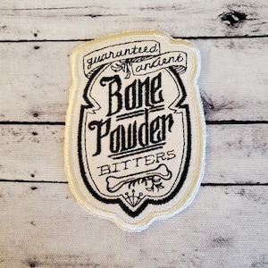 May include: White embroidered patch with black lettering that reads "guaranteed ancient Bone Powder Bitters".