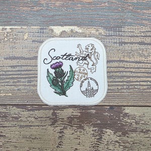 May include: Square patch with embroidered Scotland design. Features a purple thistle, a lion, and the word "Scotland" in script. Includes text that reads "G.H. Glasgow N 24 57" and a building illustration.