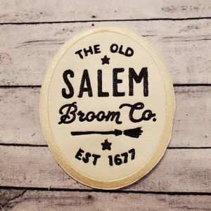 May include: A white circular patch with a gold border. The patch has black text that reads "The Old Salem Broom Co. Est 1677" with a star and a broom graphic.