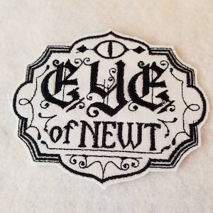 May include: Black and white embroidered patch with an eye and the text "Eye of Newt".