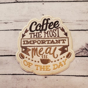 May include: Beige embroidered patch with brown stitching. The patch features the text "Coffee the most important meal of the day" with a coffee cup graphic.
