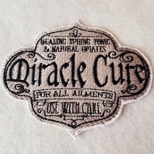 May include: A white embroidered patch with black text that reads "Healing Spring Tonic & Natural Opiates Miracle Cure For All Ailments Use With Care".