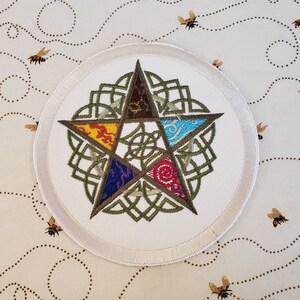 May include: A white round patch with a green Celtic knot design surrounding a five-pointed star. The star is divided into five sections, each with a different color and pattern: red, orange, yellow, blue, and purple.