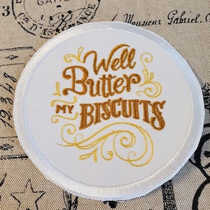 May include: White round embroidered patch with gold lettering that reads "Well Butter My Biscuits".