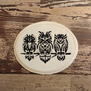 May include: A white circular patch with three black embroidered owls perched on a branch. The owls have detailed patterns and are facing forward.