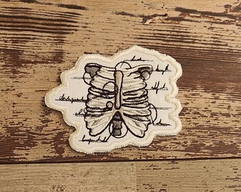 May include: A beige embroidered patch with a detailed anatomical illustration of a rib cage. The patch has a white background with black lines and text.