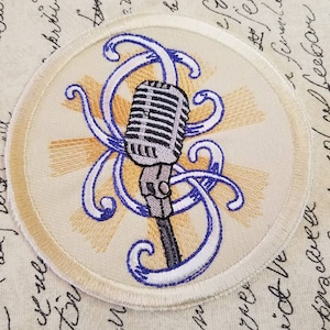 May include: A white embroidered patch with a vintage microphone and blue and yellow swirls. The microphone is silver and gray with a black cord.