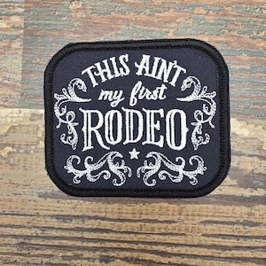 May include: A white ceramic mug with a black handle and the text "But First, Coffee" in a bold, black font. The mug is set against a blurred background, suggesting a cozy setting.