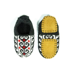May include: A pair of black knitted slippers with a white and red geometric pattern. The slippers have a brown suede patch on the bottom.