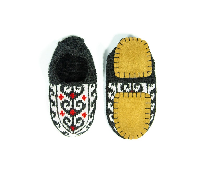 May include: A pair of black knitted slippers with a white and red geometric pattern. The slippers have a brown suede patch on the bottom.