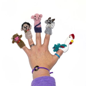 May include: Five finger puppets made of crocheted yarn, depicting a cow, a sheep, a goat, a rooster, and a pig. The puppets are worn on a person's fingers.