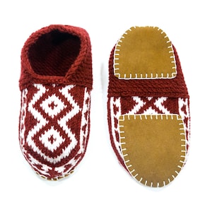 May include: A pair of red knitted slippers with white geometric patterns and brown suede soles. The slippers have a closed toe and a rounded shape.