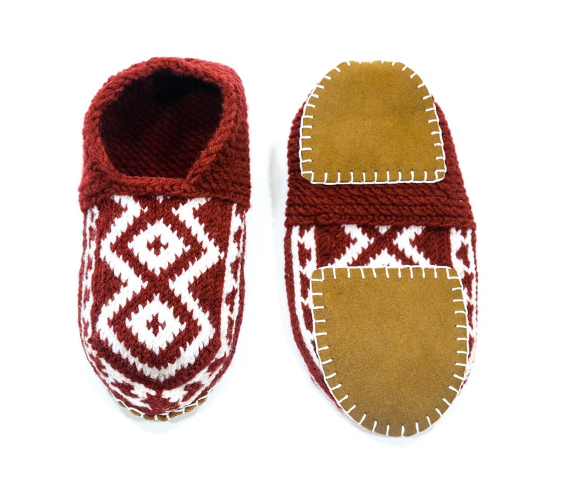 May include: A pair of red knitted slippers with white geometric patterns and brown suede soles. The slippers have a closed toe and a rounded shape.