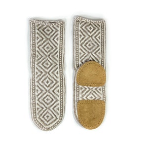 May include: A pair of beige knitted slipper socks with a geometric pattern and brown leather soles.