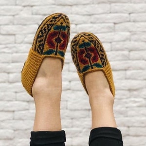 May include: A pair of knitted slippers with a geometric pattern in shades of brown, red, and green. The slippers are made of a soft, warm material and are perfect for keeping your feet cozy.