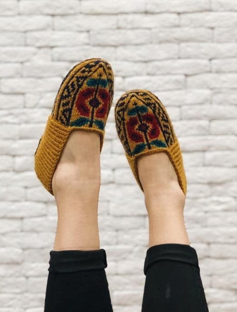 May include: A pair of knitted slippers with a geometric pattern in shades of brown, red, and green. The slippers are made of a soft, warm material and are perfect for keeping your feet cozy.