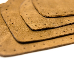 May include: Four brown leather patches with holes punched around the edges, stacked on top of each other.