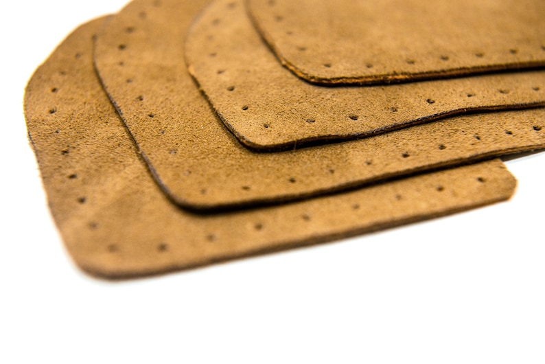 May include: Four brown leather patches with holes punched around the edges, stacked on top of each other.