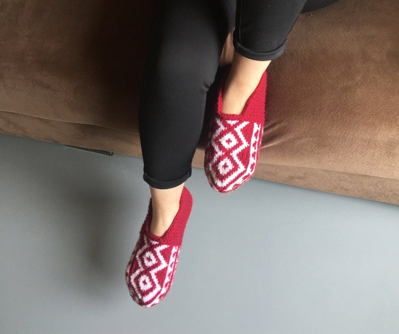 May include: Red and white knitted slippers with a geometric pattern. The slippers are worn on a person's feet.