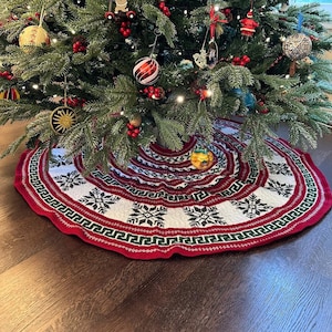 May include: A red, white, and green knitted Christmas tree skirt with a snowflake pattern. The skirt is decorated with a red, white, and green border.