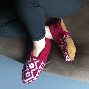 May include: Red and white knitted slippers with a brown suede sole. The slippers have a geometric pattern.