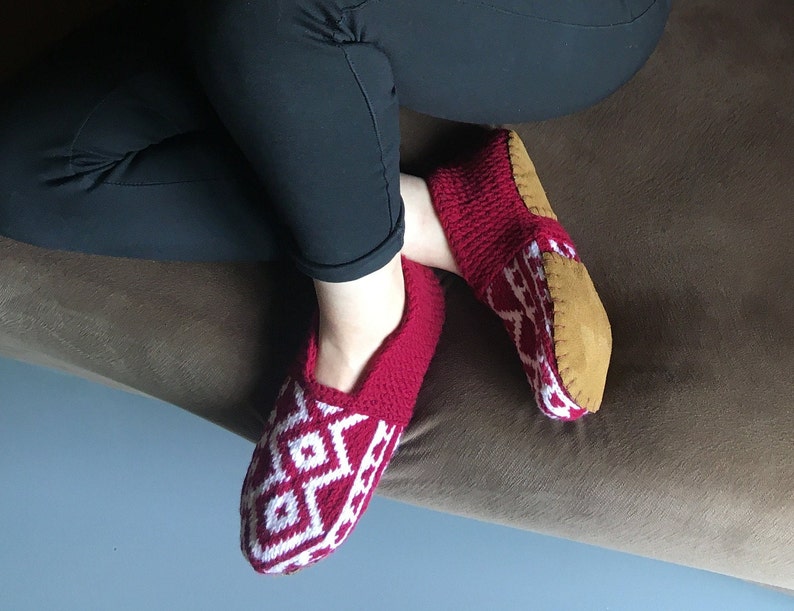 May include: Red and white knitted slippers with a brown suede sole. The slippers have a geometric pattern.