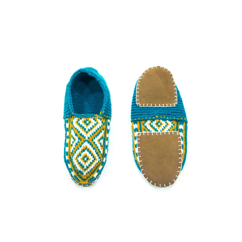 May include: A pair of teal blue crocheted slippers with a geometric pattern in white and gold. The slippers have a brown suede insole.
