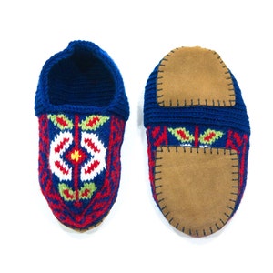 May include: A pair of blue knitted slippers with red, white, and green floral embroidery. The slippers have brown suede soles.