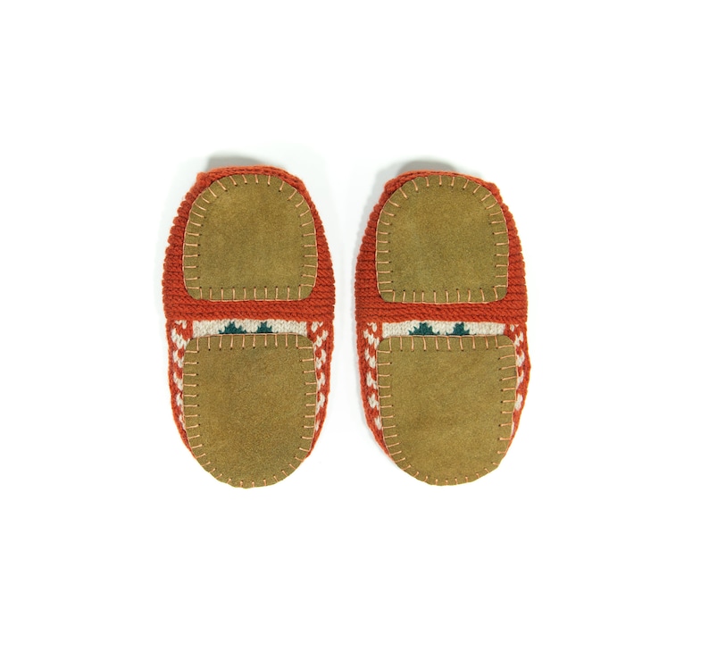 May include: A pair of red knitted slippers with brown suede soles. The slippers have a white and green geometric pattern.