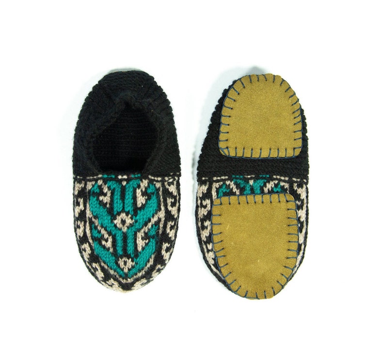 May include: A pair of black knitted slippers with a teal and beige geometric pattern. The slippers have a suede sole with a stitched edge.
