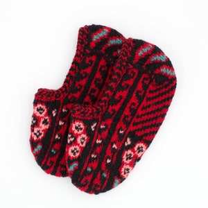 May include: A pair of red and black knitted slipper socks with a geometric pattern. The socks have a floral design with pink, blue, and green accents.