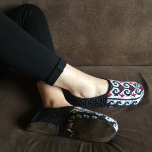 May include: A pair of black and white knitted slippers with red accents. The slippers have a brown suede sole.