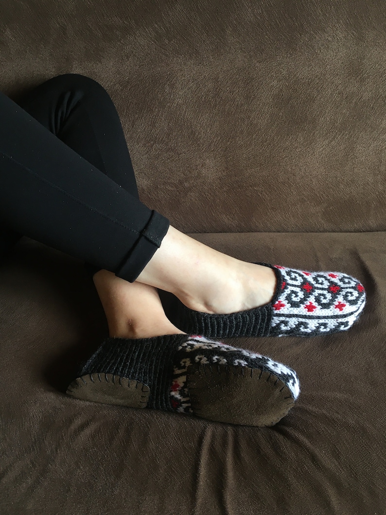May include: A pair of black and white knitted slippers with red accents. The slippers have a brown suede sole.