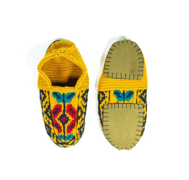 May include: A pair of yellow knitted slippers with colorful geometric patterns and brown leather soles.