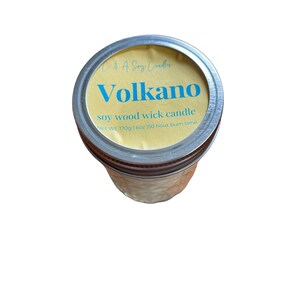 May include: A yellow and blue soy wood wick candle in a glass jar with a silver lid. The label reads "Volkano soy wood wick candle Net Wt. 170g | 6oz 150 hour burn time".