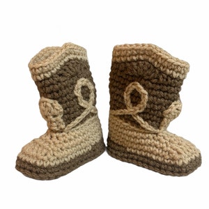 Può includere: Un paio di scarpine per neonati all'uncinetto in marrone e beige con un design a stivale da cowboy.