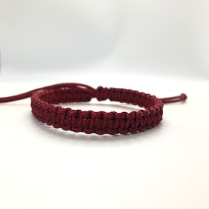May include: A dark red braided bracelet with a simple knot closure.