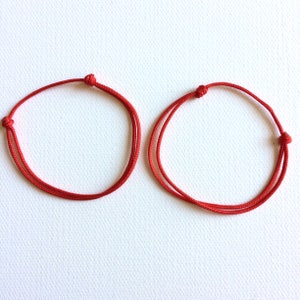 May include: Two red string bracelets, tied in a simple knot, on a white background.