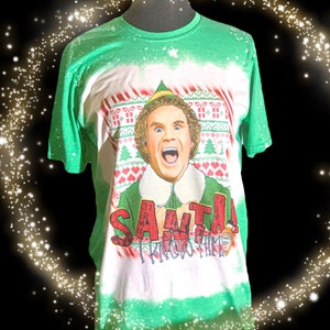 May include: Green and white t-shirt featuring a graphic of a character from the movie "Elf". The character is wearing an elf hat and collar, with the text "SANTA! I KNOW HIM!" in red. The shirt has a Christmas sweater design.