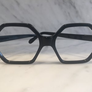 May include: Black hexagonal-shaped eyeglasses with a dark frame and clear lenses.