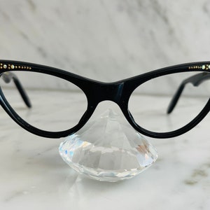 Puede incluir: Gafas de sol negras de ojo de gato con pedrería en las patillas.