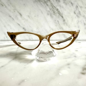 Op de afbeelding: Een paar bruine cat-eye brillen met heldere glazen, rustend op een kristalvormig diamantvormig object.